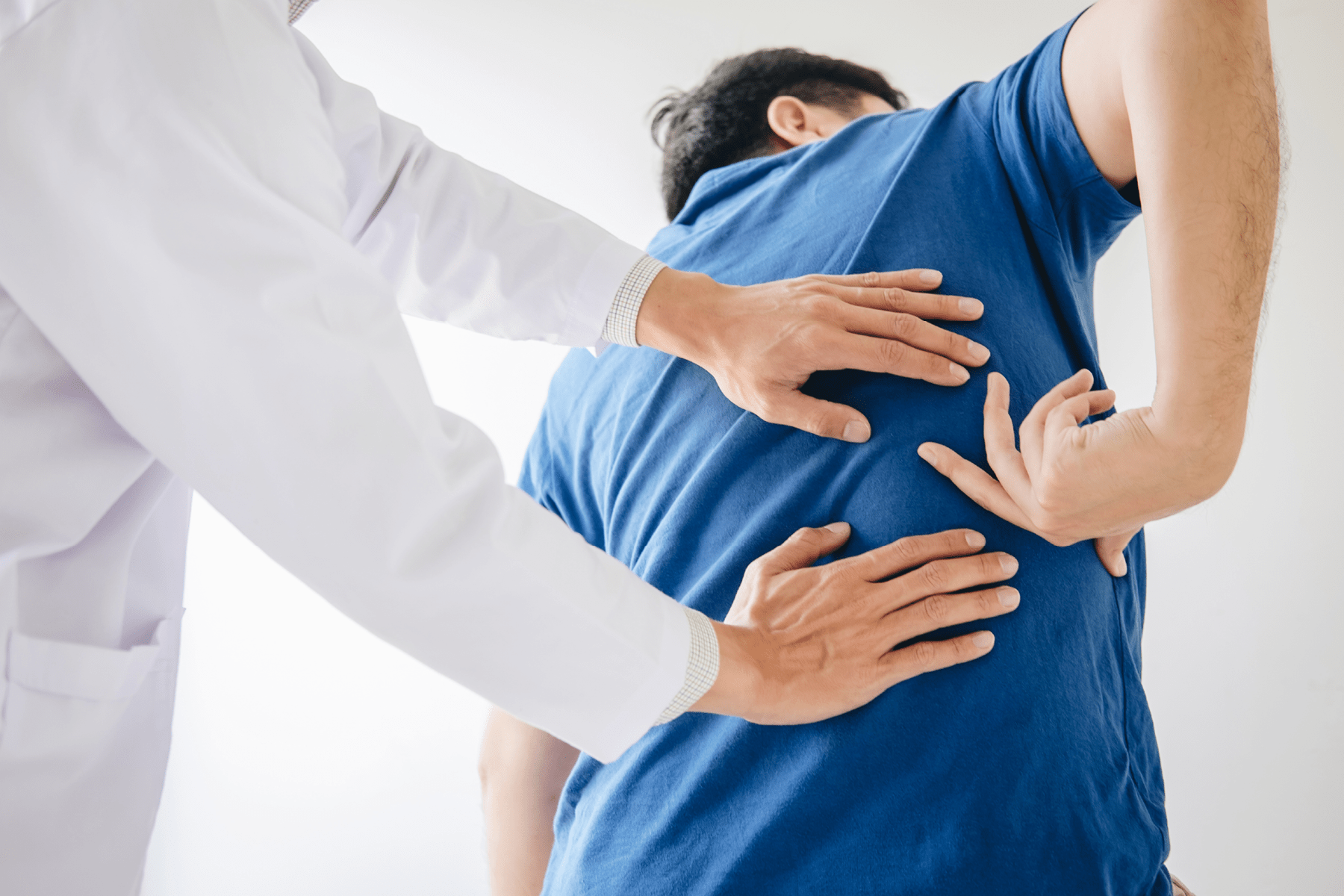 A doctor touching a patients back with both hand where the patient is pointing.
