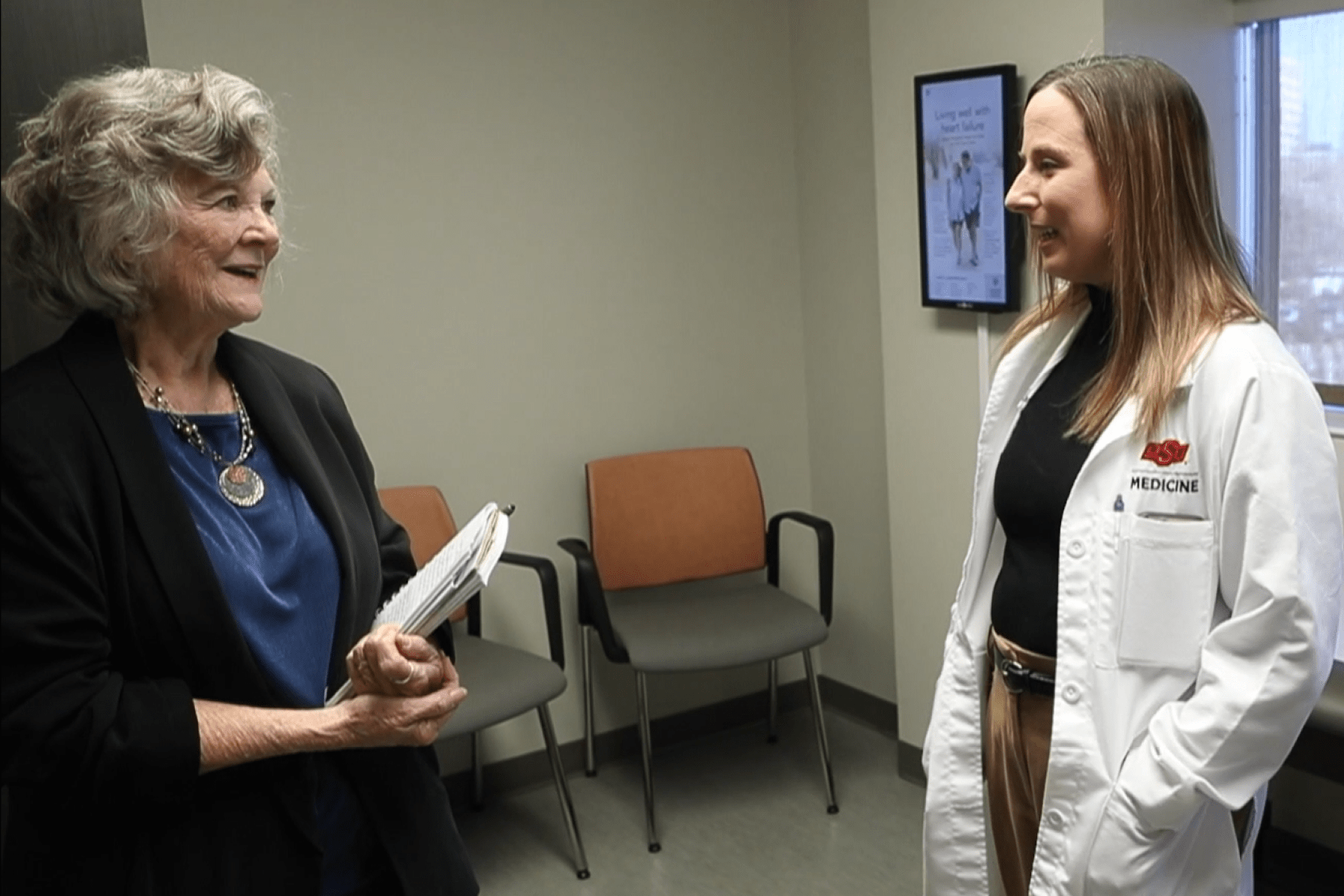 A woman speaks with a doctor in an examination room.