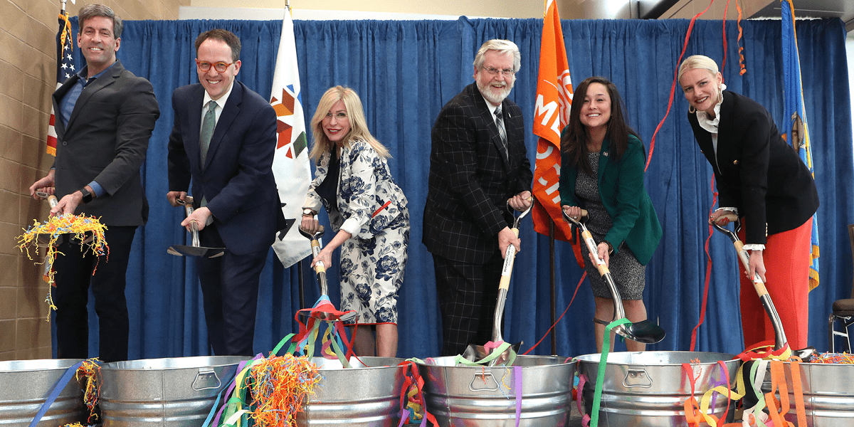 News Psych Groundbreaking City officials lift shovels out of buckets filled with confetti and streamers.