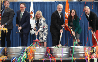 City officials lift shovels out of buckets filled with confetti and streamers.