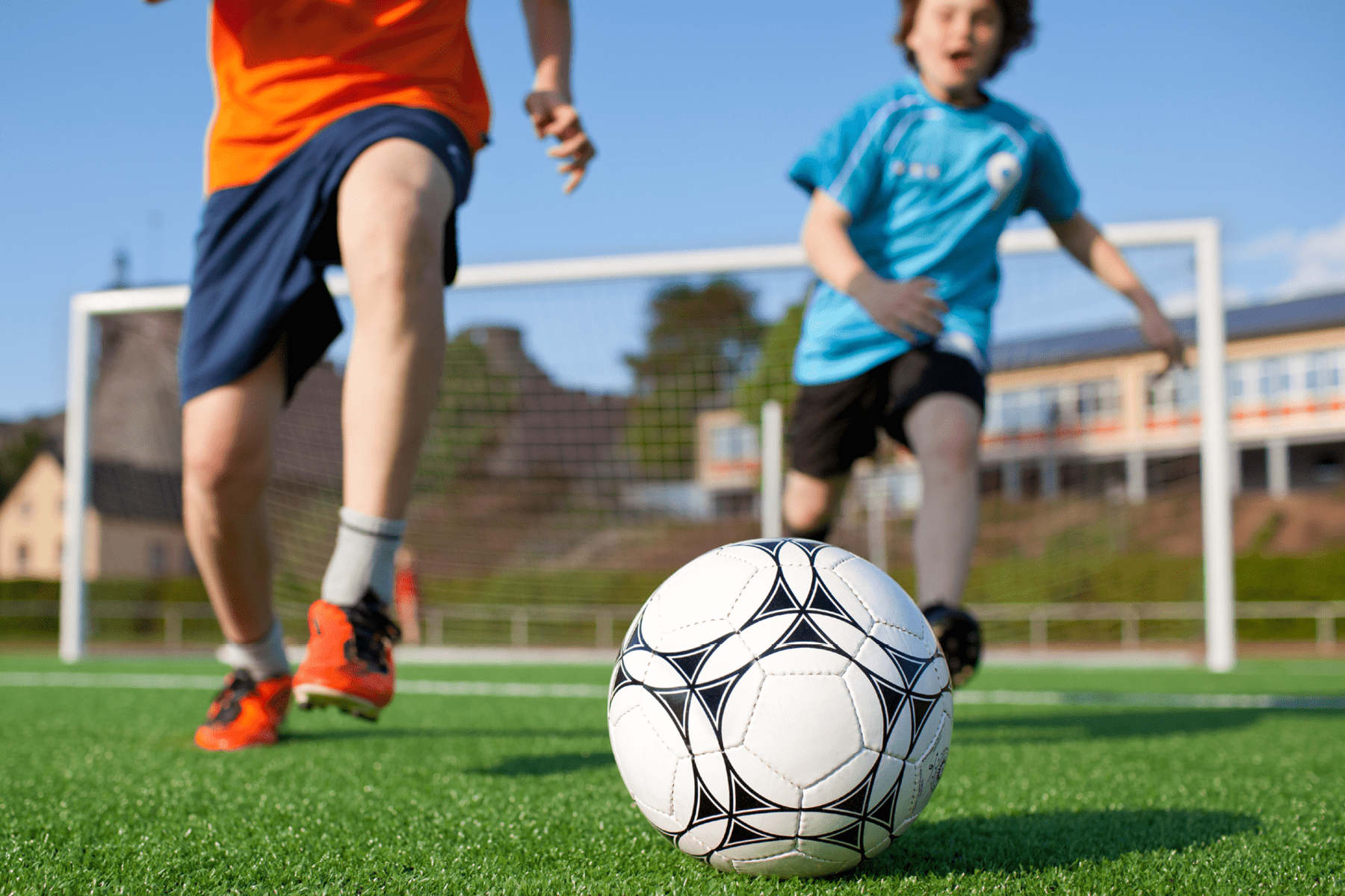Two young boys chase after a soccer ball.