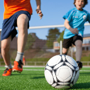 Care Connections Vertical – Sports Two young boys chase after a soccer ball.