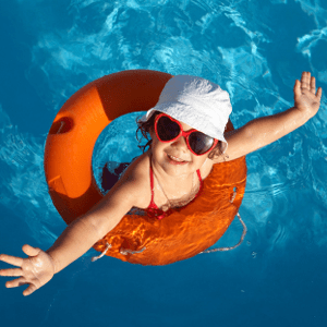 A child wearing heart shaped sun glasses wades in a pool using an orange floatation device.