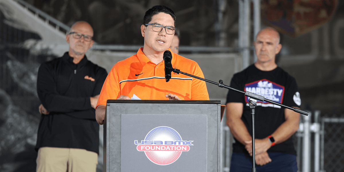 BMX-hz A man speaking at a podium with three men standing behind him.