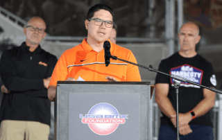 A man speaking at a podium with three men standing behind him.
