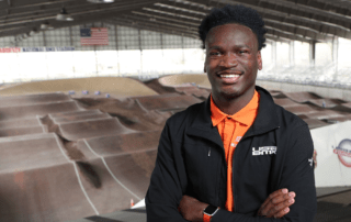 A man stands smiling with his arms folded and a BMX track in the background.