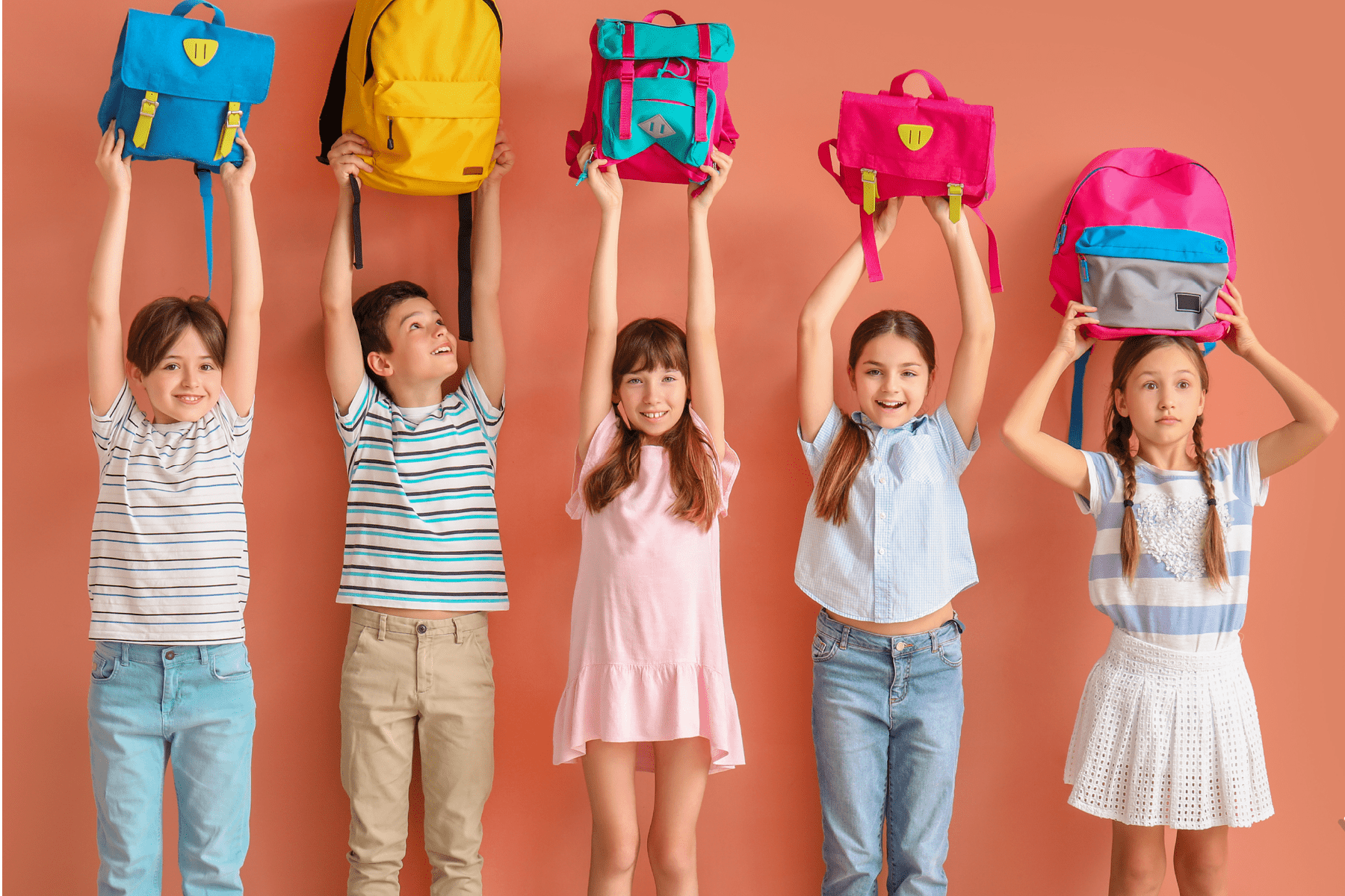 Five children in colorful clothing raise their backpacks above their heads.