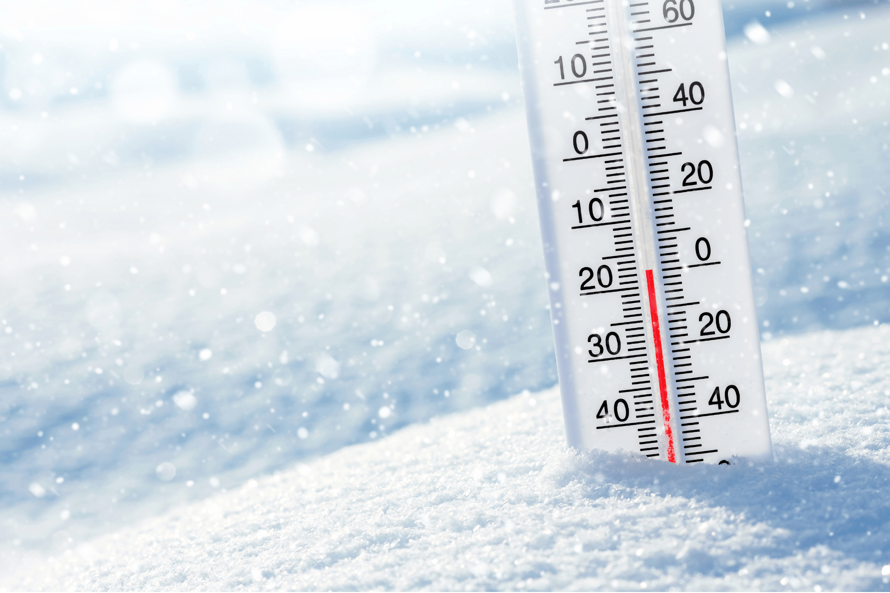 A thermometer partially buried in snow shows below freezing temperatures.