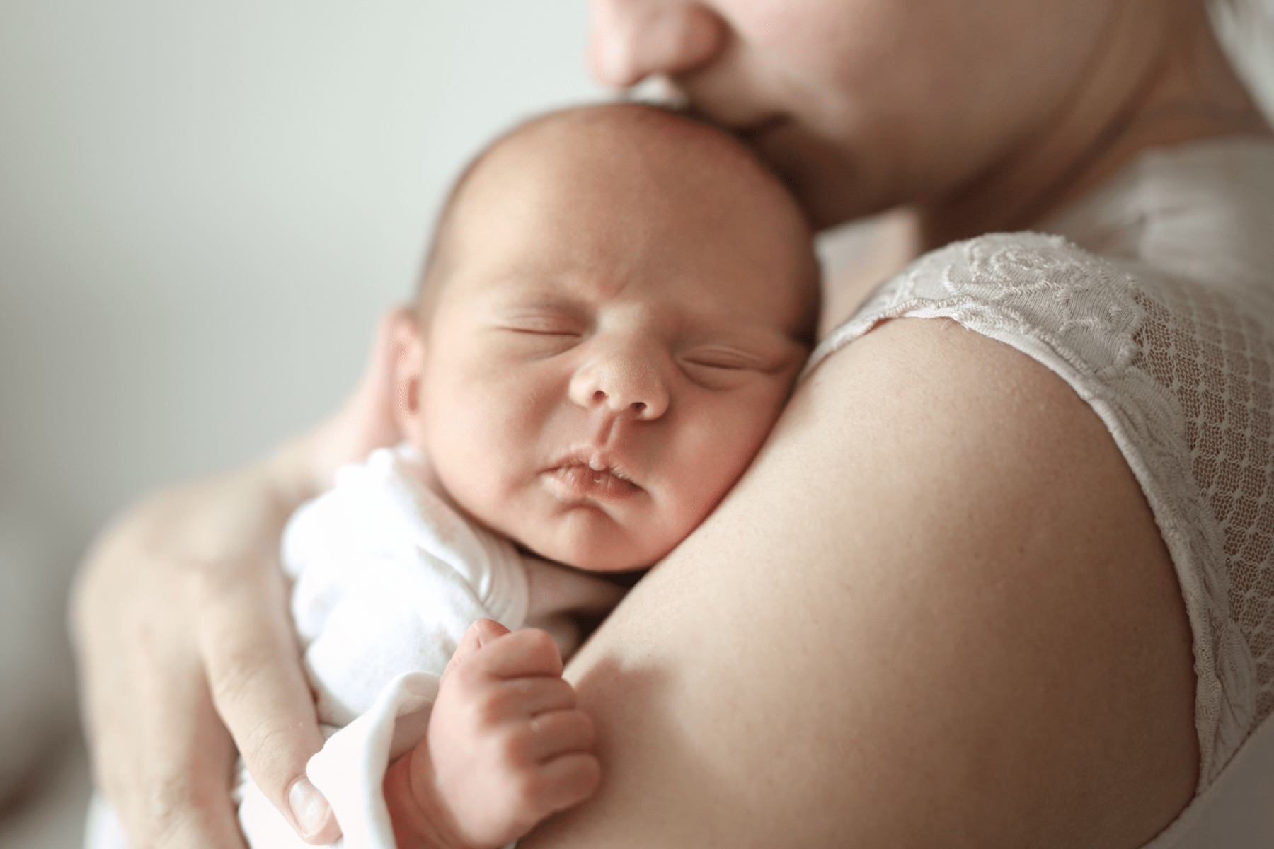 A mother holding her newborn baby close as the baby sleeps.