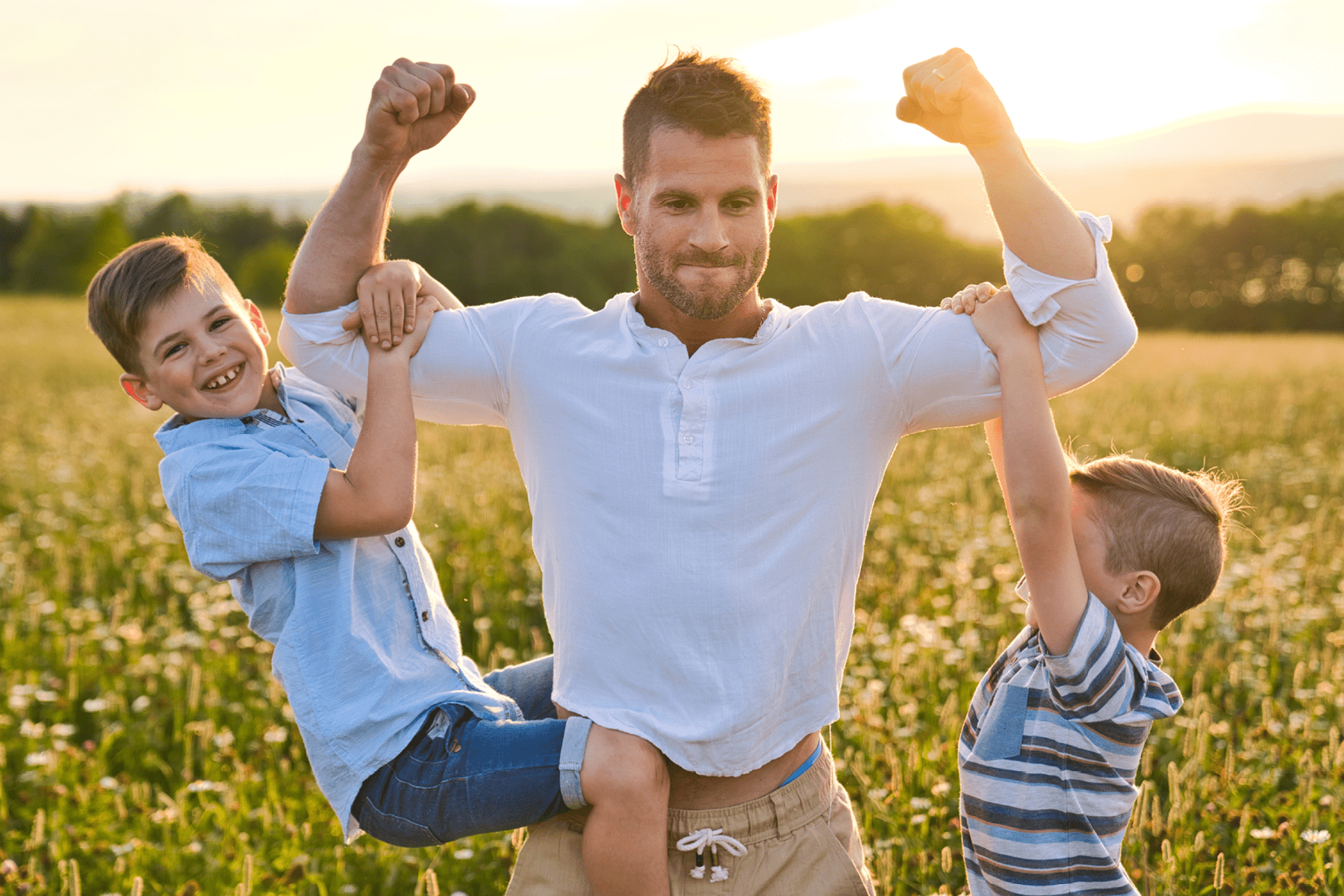 A man holding his arms up with two young boys hanging on to his biceps.